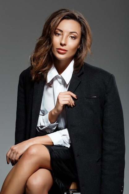 Young beautiful woman  sitting over grey wall