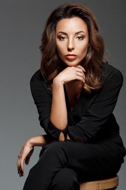 Young beautiful woman sitting over grey wall