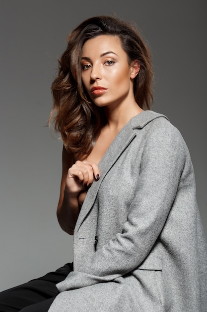 Free photo young beautiful woman sitting over grey wall