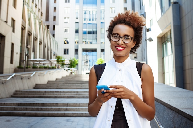 Young beautiful woman smiling holding phone walking down city