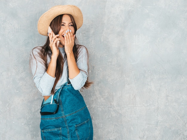 Giovane bella donna che parla sul telefono. ragazza scioccata alla moda in abiti casual e cappello di tuta estiva. divertente e sorpreso. chiudendo la bocca