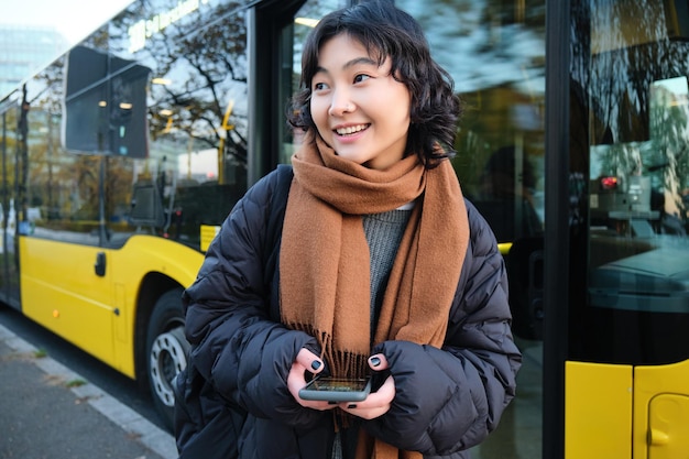 無料写真 バス停に立っている若い美しい女性携帯電話のチェックを保持しているスマート フォンでテキスト メッセージ メッセージ