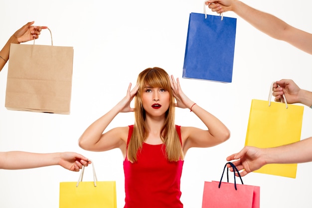 Young beautiful woman standing among purchases over white wall