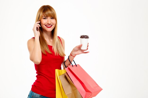 Young beautiful woman standing with purchases over white wall