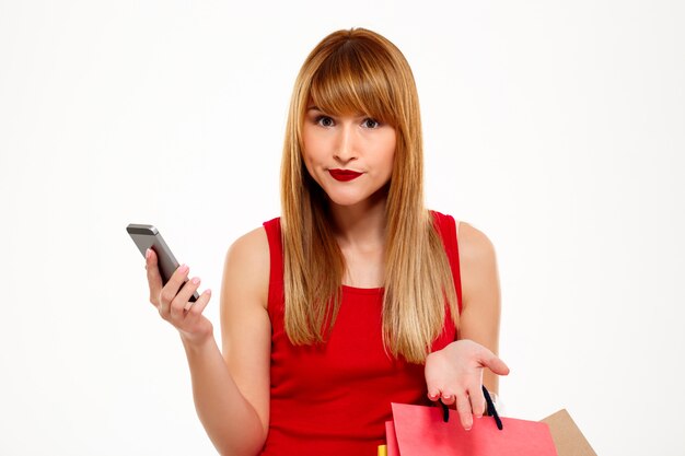 Young beautiful woman standing with purchases over white wall