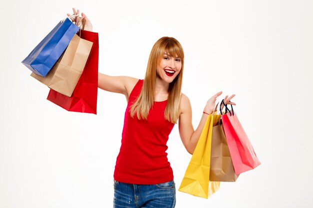 Young beautiful woman standing with purchases over white wall