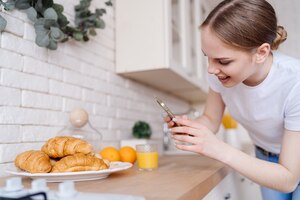 young beautiful woman taking photo on mobile phone of croissants