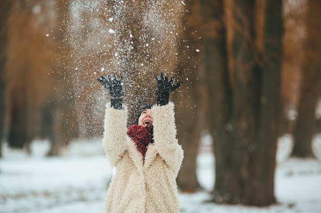 若い美しい女性が頭の上に雪を投げる