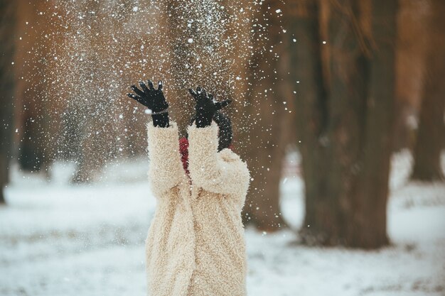 若い美しい女性が頭の上に雪を投げる