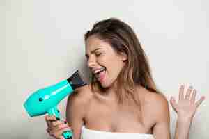 Free photo young beautiful woman in towel singing with hairdryer