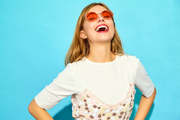 Young beautiful woman .Trendy woman in casual summer clothes in sunglasses. Positive female emotion facial expression body language. Funny model isolated on blue wall