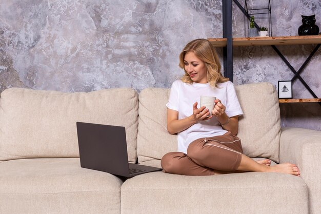 Young beautiful woman using laptop computer smiling happy watching and browsing or doing online internet shopping at home. Modern living room. Cheerful and satisfied face expression