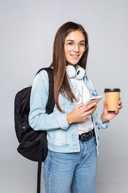 Молодая красивая женщина, используя смартфон с кофе, изолированных на белой стене