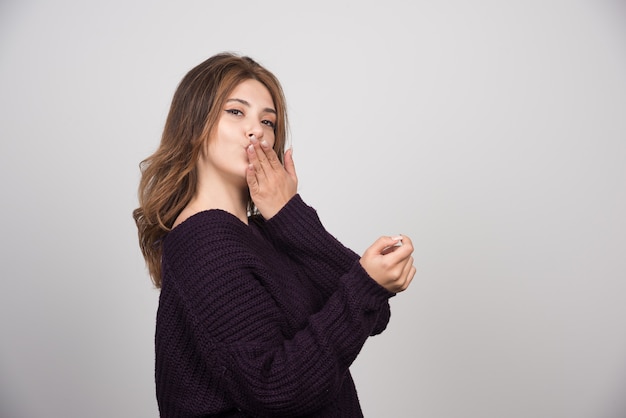 Young beautiful woman in warm knitted sweater blowing an air kiss.