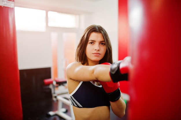 젊고 아름다운 여성은 권투 장갑을 끼고 운동을 하고 체육관에서 열심히 일하고 훈련 과정을 즐깁니다.