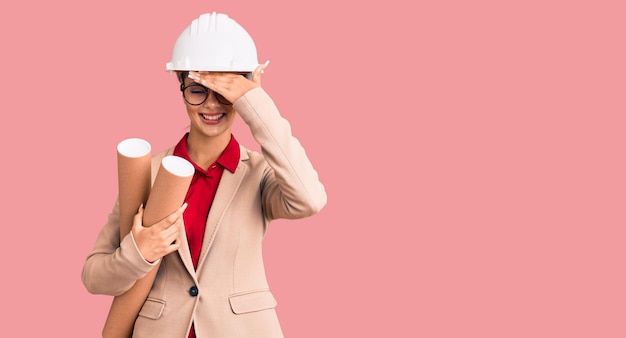 Foto gratuita giovane bella donna che indossa elmetto protettivo da architetto e occhiali con progetti stressati e frustrati con la mano sulla testa, faccia sorpresa e arrabbiata