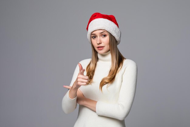 앞을 가리키는 외진 벽 위에 크리스마스 모자를 쓰고 있는 젊은 아름다운 여성