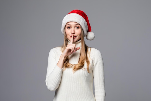 Молодая красивая женщина в шляпе Рождества Санта-Клауса над изолированной белой стеной просит молчать с пальцем на губах