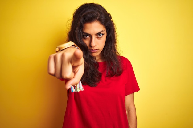 Бесплатное фото Молодая красивая женщина в красной футболке, стоящая на изолированном желтом фоне, указывая пальцем на камеру, а вам показывает позитивный и уверенный жест спереди