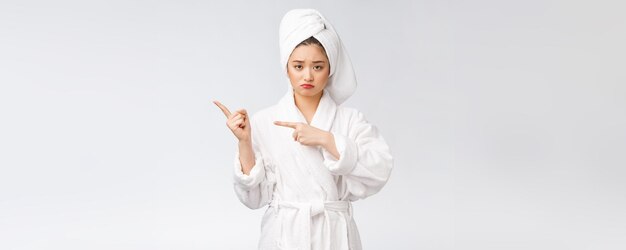 손가락으로 가리키는 고립 된 흰색 배경 위에 목욕 후 샤워 타월을 착용 하는 젊은 아름 다운 여자