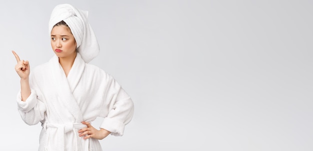 손가락으로 가리키는 고립 된 흰색 배경 위에 목욕 후 샤워 타월을 착용 하는 젊은 아름 다운 여자