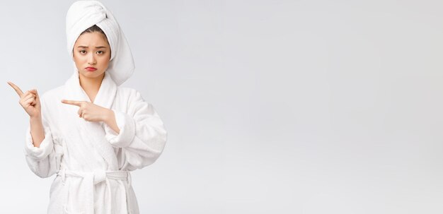 指で指している孤立した白い背景の上に風呂の後にシャワータオルを着ている若い美しい女性