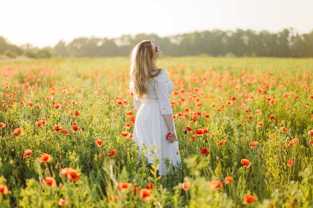 Молодая красивая женщина в белом платье позирует в маковом поле