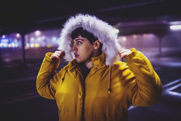 Young beautiful woman wearing a yellow winter coat with a blurred city at night