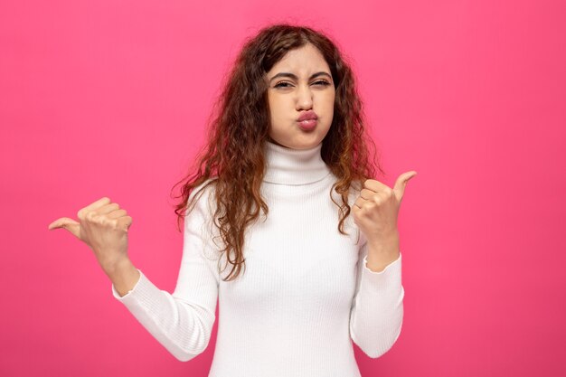 Young beautiful woman in white turtleneck blowing on nails standing on pink