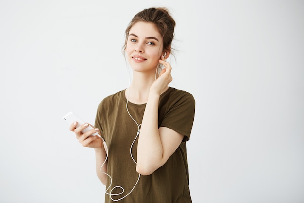 Бесплатное фото Молодая красивая женщина с музыкой плюшки усмехаясь слушая в наушниках над белой предпосылкой.