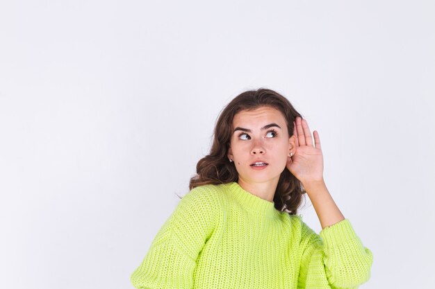 Young beautiful woman with freckles light makeup in sweater on white wall gossip talk listen secret