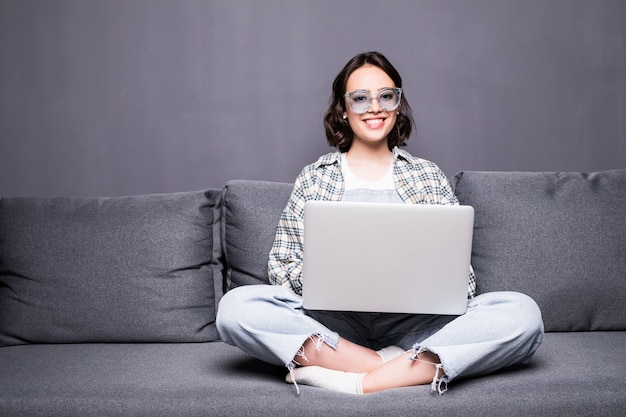 Young beautiful woman with glasses using a laptop computer at home sitting on sofa