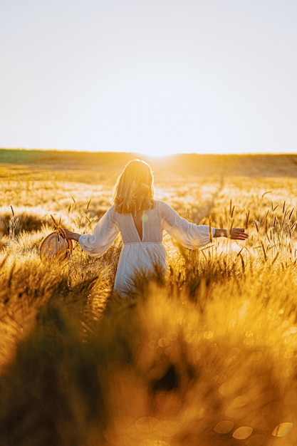 日の出の早朝の麦畑で白いドレスを着た長いブロンドの髪を持つ若い美しい女性。夏は夢想家、空飛ぶ髪、光線の中でフィールドを横切って走っている女性のための時間です