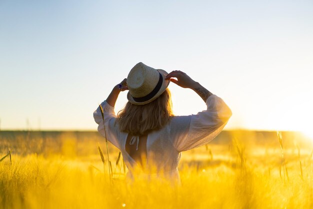 日の出の早朝の麦畑で白いドレスを着た長いブロンドの髪を持つ若い美しい女性。夏は夢想家、空飛ぶ髪、光線の中でフィールドを横切って走っている女性のための時間です