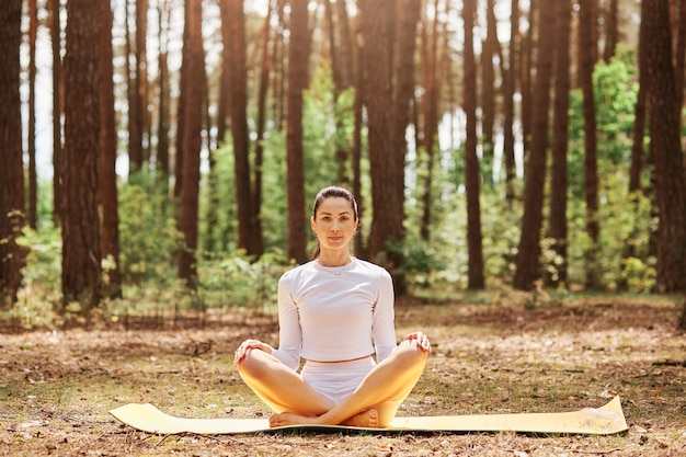 Young beautiful woman with pleasant appearance sitting on karemat in yoga pose