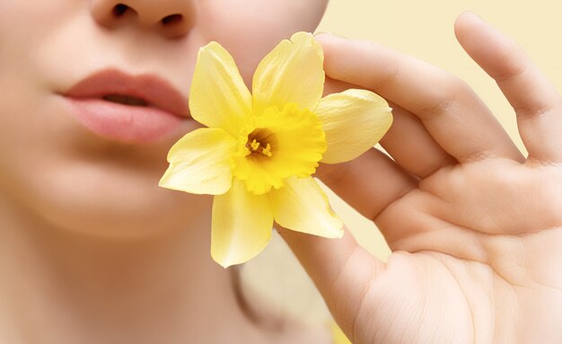 Young beautiful woman with yellow narcissus flower, close up.