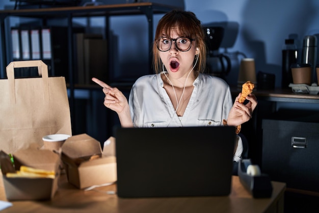 young-beautiful-woman-working-using-computer-laptop-eating-delivery-food-surprised-pointing-with-finger-side-open-mouth-amazed-expression_839833-6488.jpg