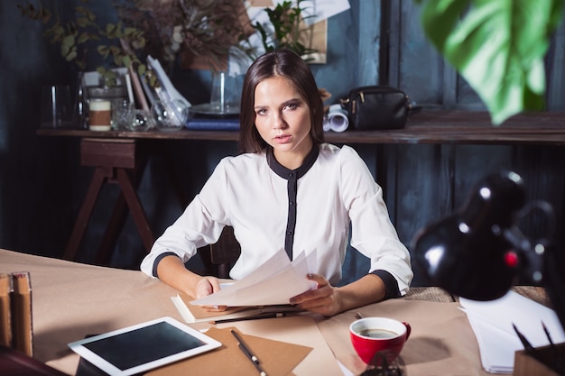 ロフトオフィスでコーヒーとノートブックを操作する若い美しい女性