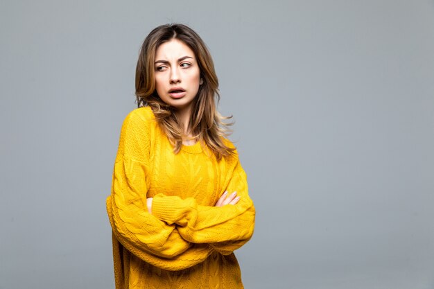 Young beautiful woman in yellow casual sweater standing with arms crossed isolated on gray wall