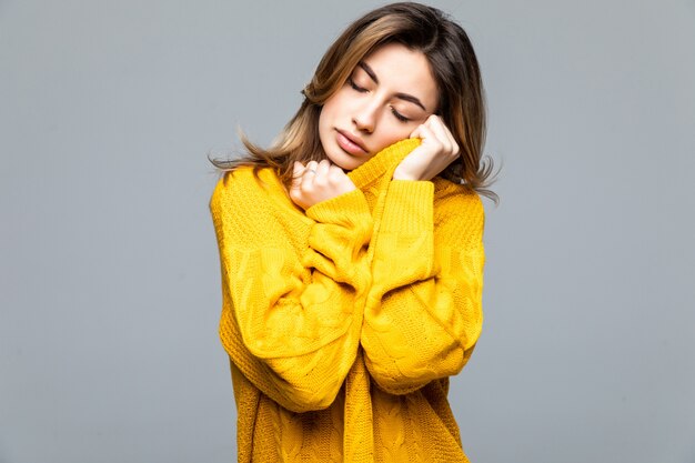 Young beautiful woman in yellow casual sweater standing with arms crossed isolated on gray wall