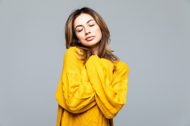 Young beautiful woman in yellow casual sweater standing with arms crossed isolated on gray wall