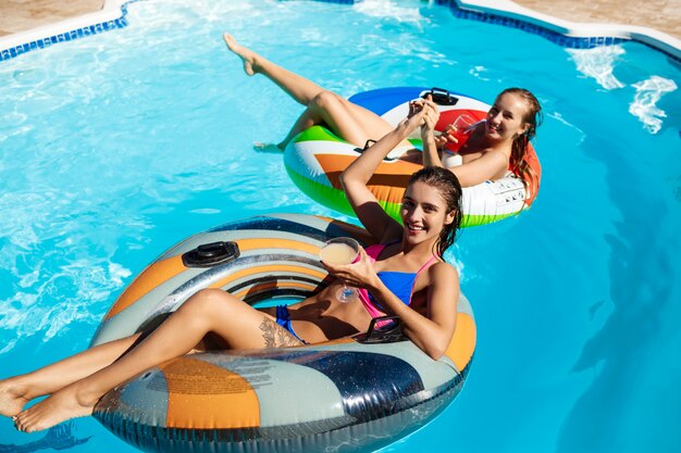 Young beautiful women smiling, sunbathing, relaxing, swimming in pool