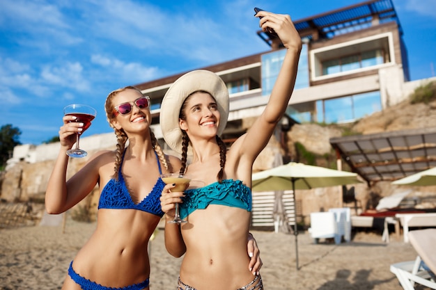 Young beautiful women in swimwear smiling, making selfie at beach