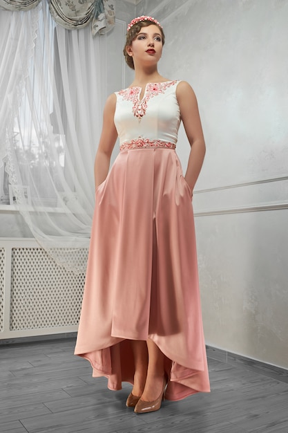 Young beauty, pretty woman in peach long dress, hand on hip, loo