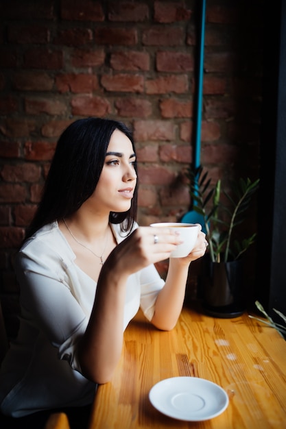 Молодая женщина красоты пьет кофе в кафе на открытом воздухе.
