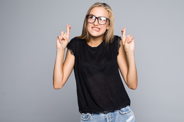 Young beauty woman keeps fingers crossed, hopes for good luck, isolated against gray background with copy space for your text or advertisment