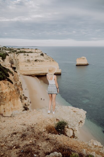 Young beauty Woman in straw hat enjoying great view on the rocky coastline during the sunrise