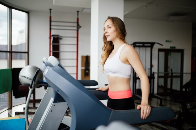 Young beauty woman working out on run simulator in sport gym club.