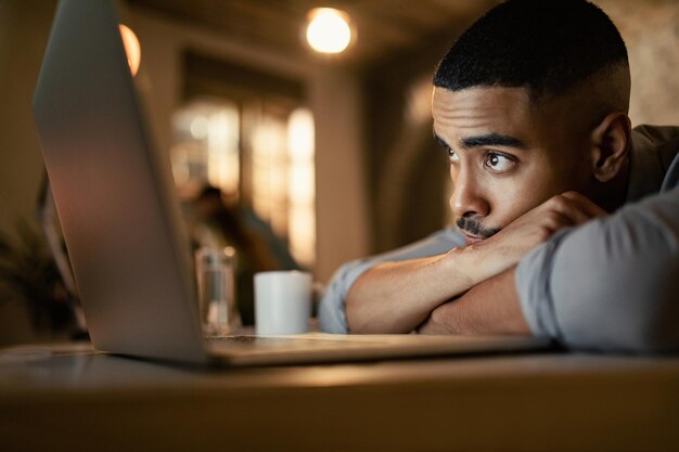 Young black businessman leaning on his desk while working on a computer at night