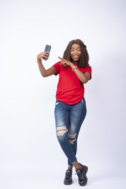 Молодая чернокожая дама держит свой телефон и с волнением на лице указывает на него